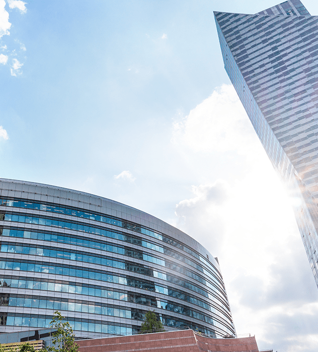 looking up at a large round office building next to a skyscraper on a sunny day
