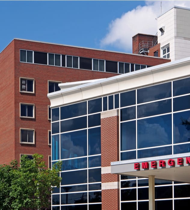 red brick hospital building from a distance with an emergency sign