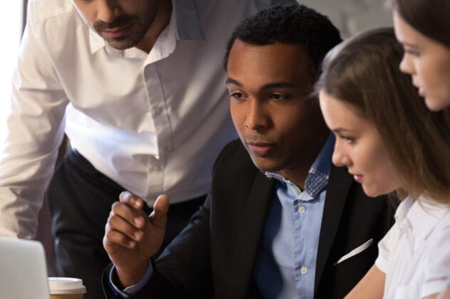 two men and two women in business wear looking at a laptop and performing website accessibility audits