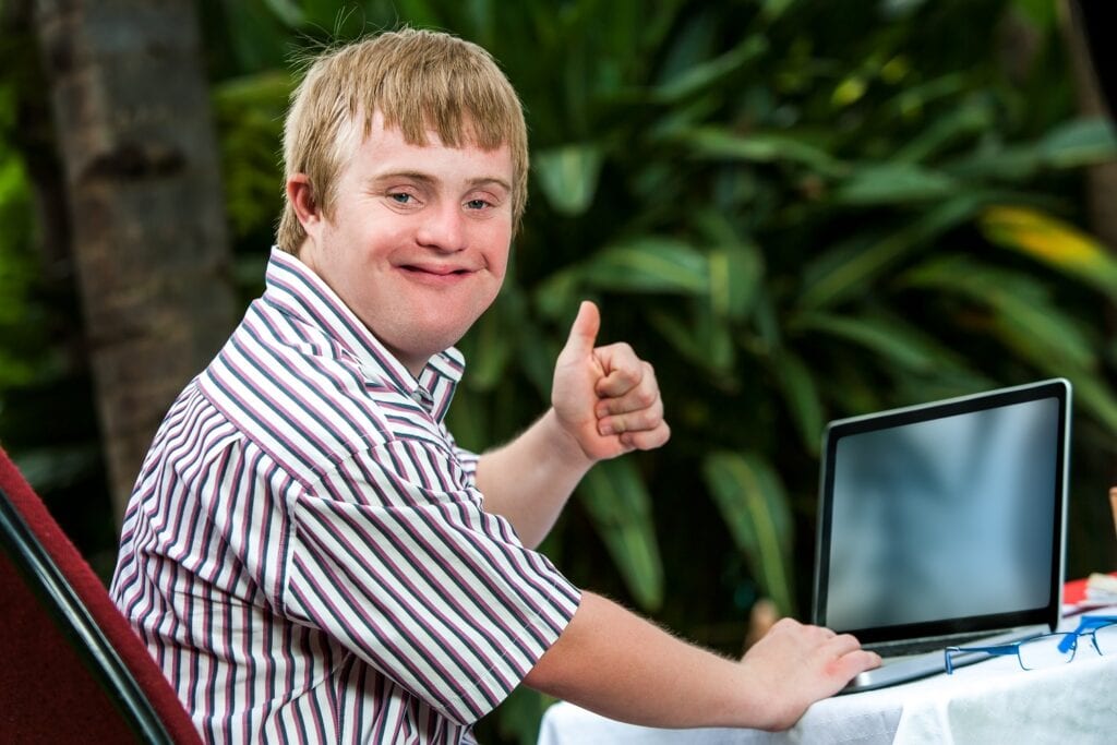 Young man with down syndrome using a laptop and giving a thumbs up.