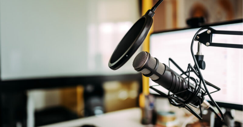 close up on a podcast microphone with a computer monitor in the background