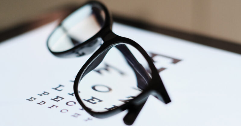 Closeup of eyeglasses set on a tablet showing an eye chart for testing vision.