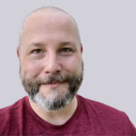 Chris Hinds is a white male in her 40's with a shaved head and beard.